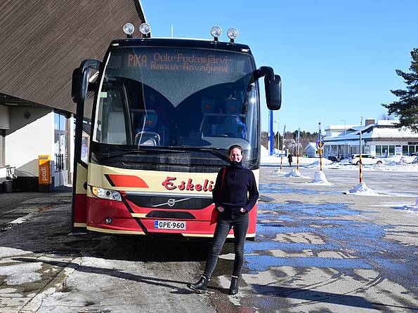 Frau steht vor Reisebus in winterlicher Landschaft Finnlands