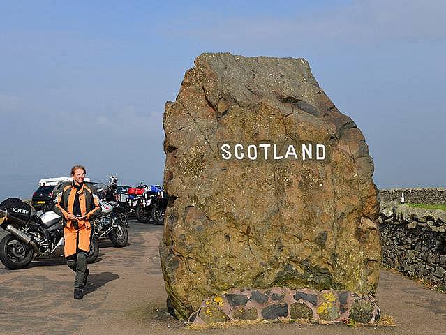 Motorräder und Motorradfahrerin an dem Grenzstein in Schottland