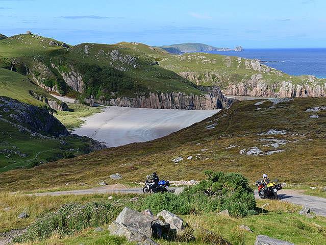 Motorräder auf Single Track vor einer Bucht mit Strand an der Nordwestküste von Schottland