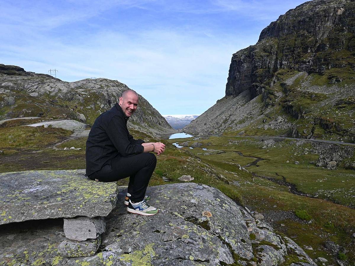 Ein Mensch sitzt auf einem Stein auf dem Røldalsfjell