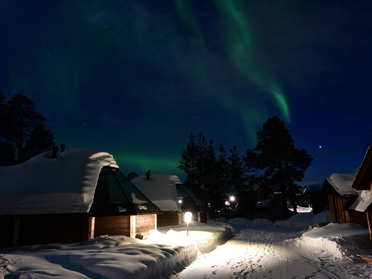 Polarlichter über Hütten in verschneiter finnischer Landschaft